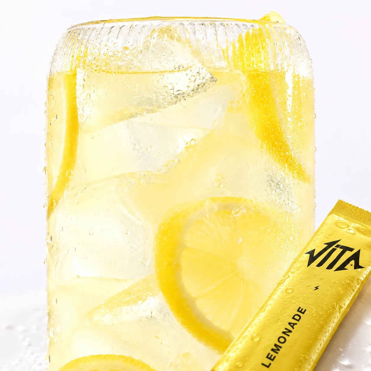 Un verre de VITA Citronnade avec glaçons et citron, à côté d’un stick